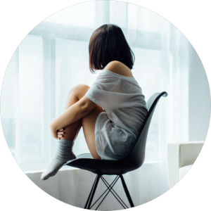 Side profile of a woman seated, holding her legs and looking out the window