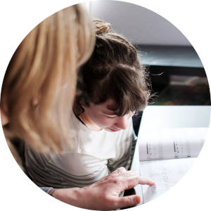 A mother and daughter seated at a desk reading a book together